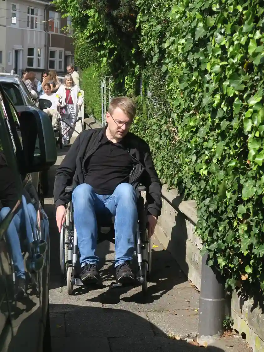 Mitglied des Beirates Schwachhausen Malte Lier beim navigieren eines Rollstuhls durch einen engen Fu&szlig;weg 