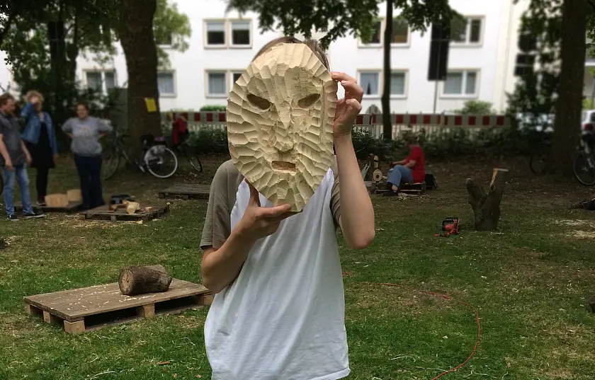 Ein Kind hält eine selbst geschnitzte Holzmaske vor sein Gesicht